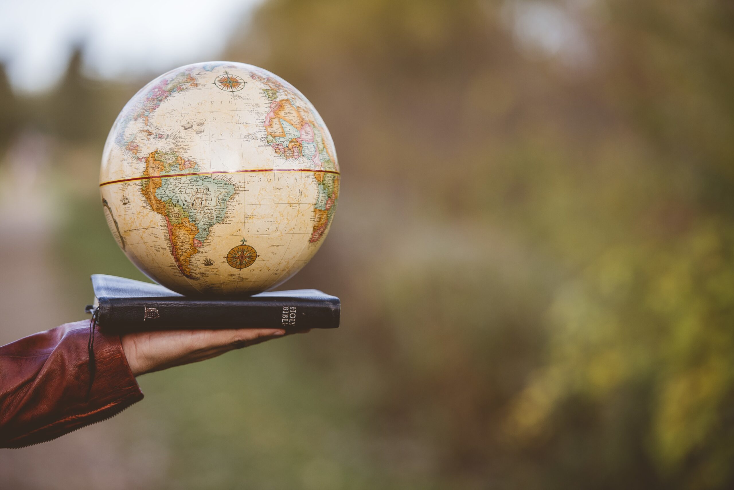 A closeup shot of a person holding bible with desk globe on top with a blurred background
